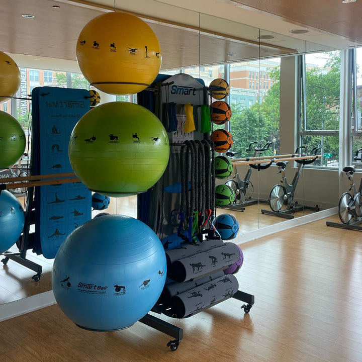 Gym interior with exercise balls and stationary bikes near large windows.